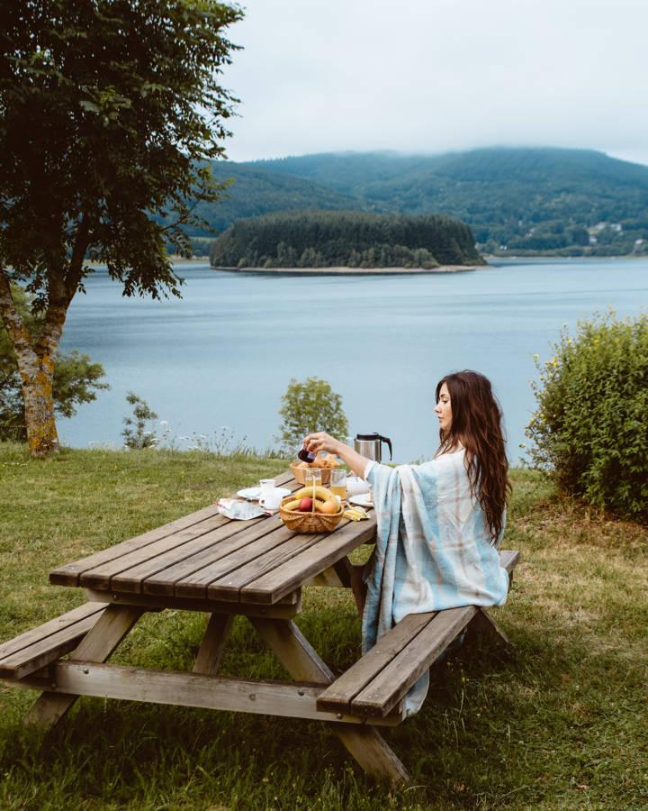 Une femmes est assise sur une table de camping au bord d'un plan d'eau