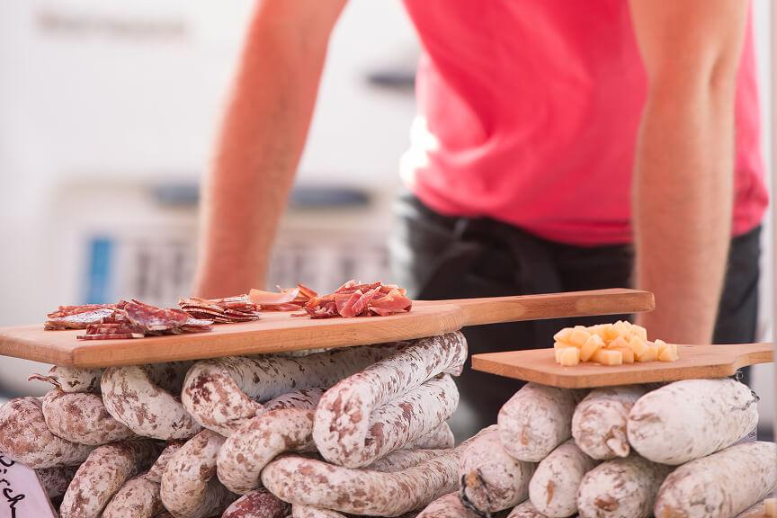 Plusieurs saucissons les uns sur les autres, une plance en bois avec des morceaux de saucissons et de frommages posée dessus